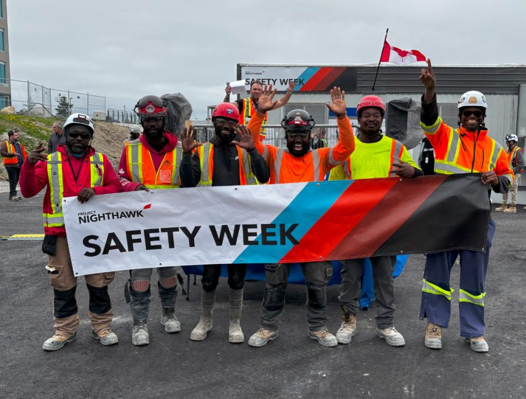 group of men standing holding a safety week banner
